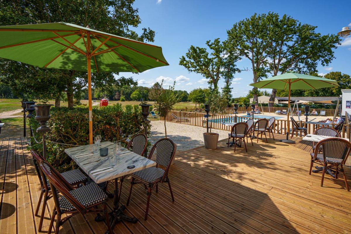une terrasse en bois avec des tables et des chaises et des parasols verts dans l'établissement Domaine de Roiffé, à Roiffé