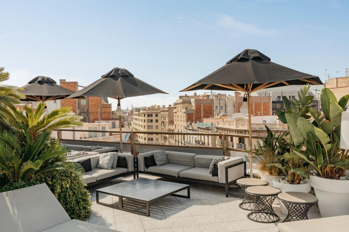 Un patio en la azotea con sofás, mesas y sombrillas. en Claris Hotel & Spa GL, a Small Luxury Hotel of the World, en Barcelona