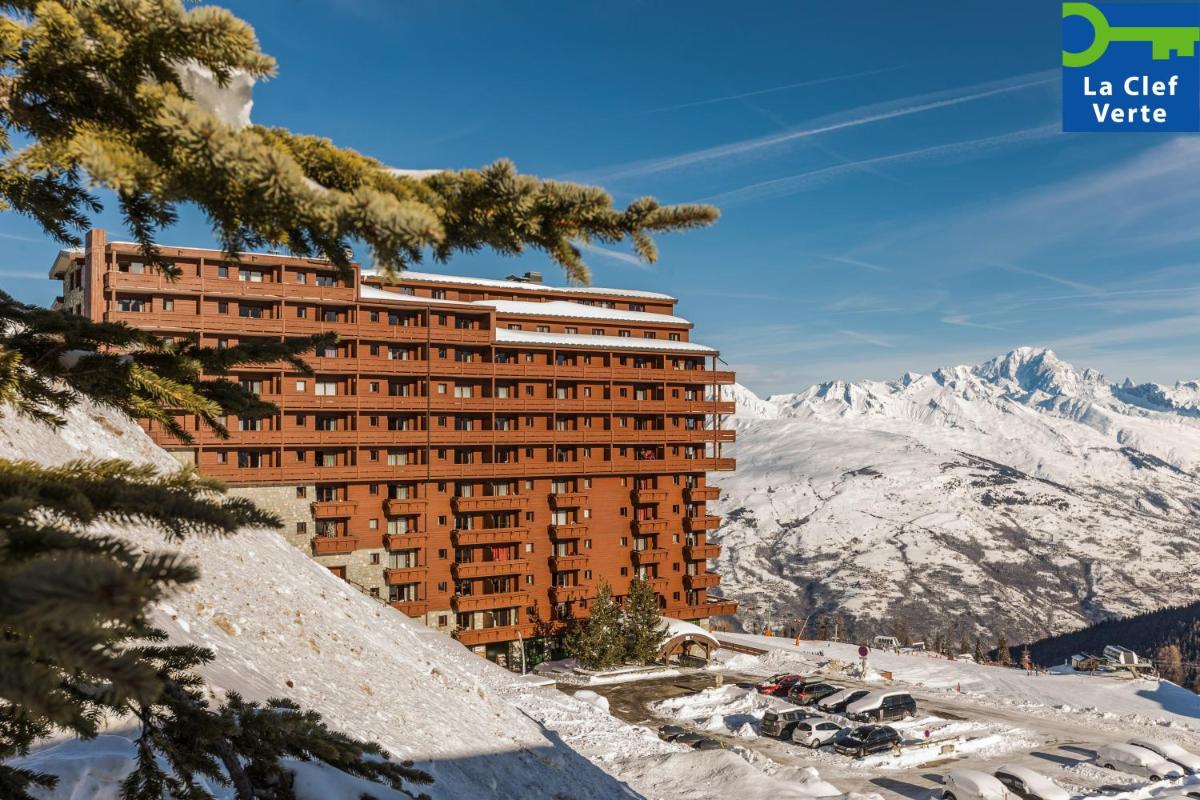 un bâtiment dans la neige avec des montagnes en arrière-plan dans l'établissement Résidence Pierre & Vacances Premium Les Hauts Bois, à Aime La Plagne