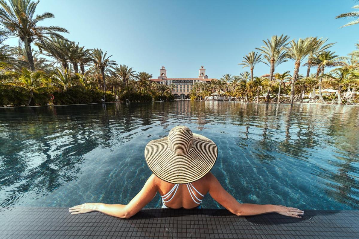 una mujer con un sombrero de paja sentada en una piscina en Unique Club at Lopesan Costa Meloneras Resort, en Maspalomas