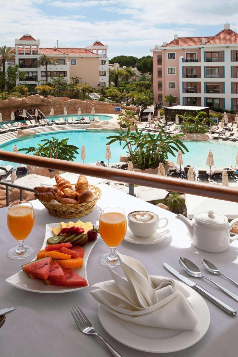 uma mesa com um prato de comida e vista para uma piscina em Hilton Vilamoura em Vilamoura