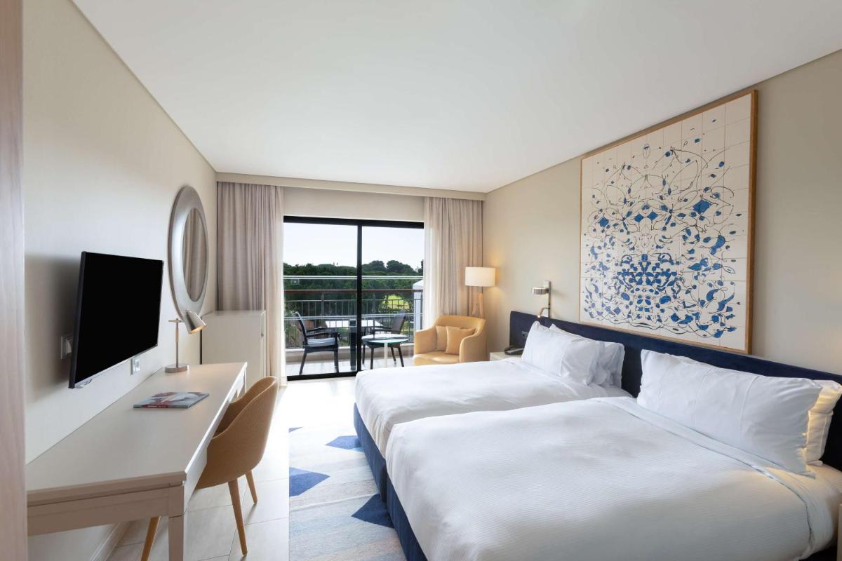 um quarto de hotel com uma cama branca e uma secretária. em Hilton Vilamoura em Vilamoura mais 84 fotografias