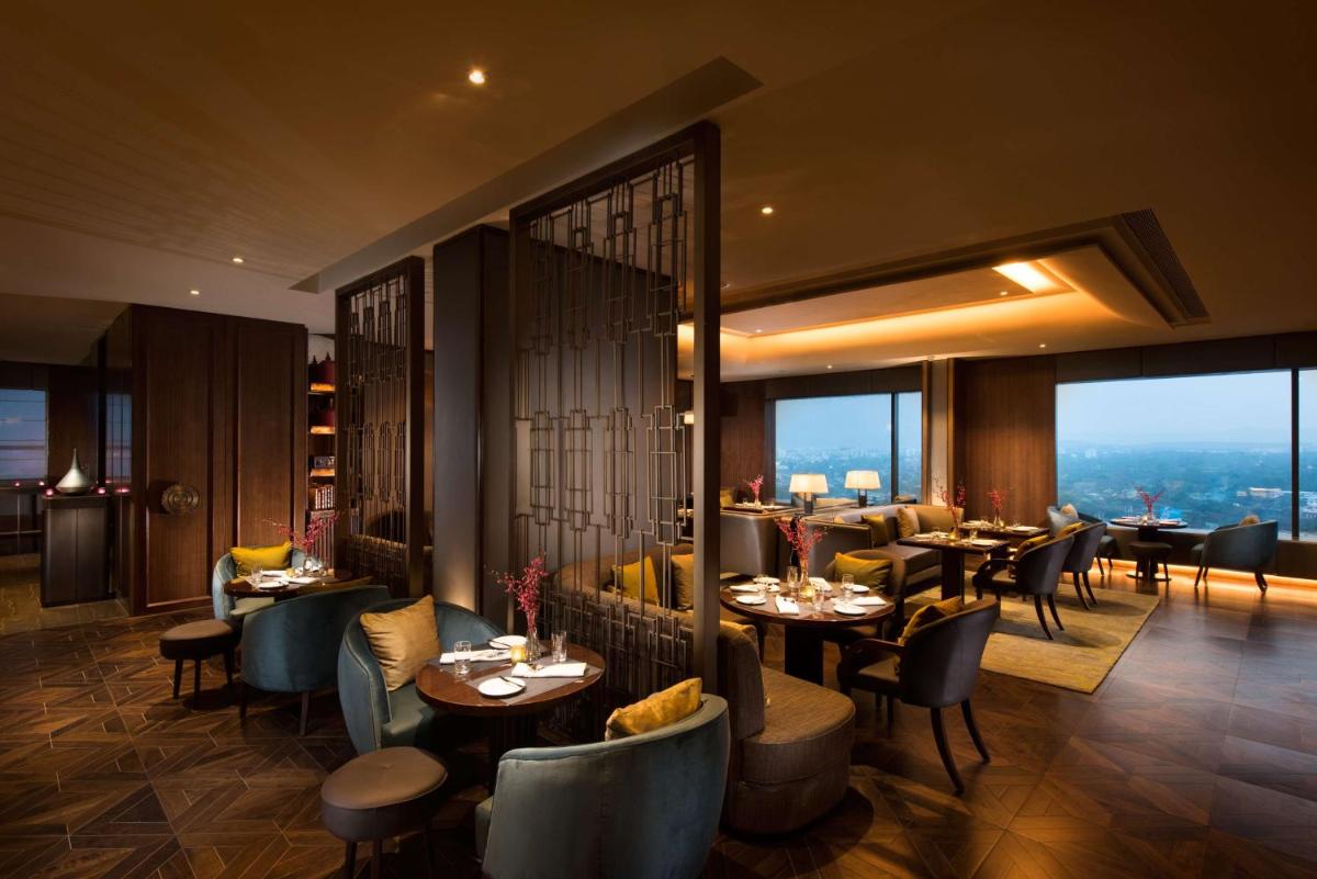 a restaurant with tables and chairs and large windows at Conrad Pune in Pune