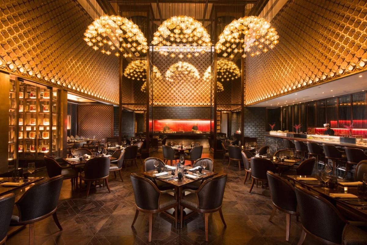 a restaurant with tables and chairs and chandeliers at Conrad Pune in Pune