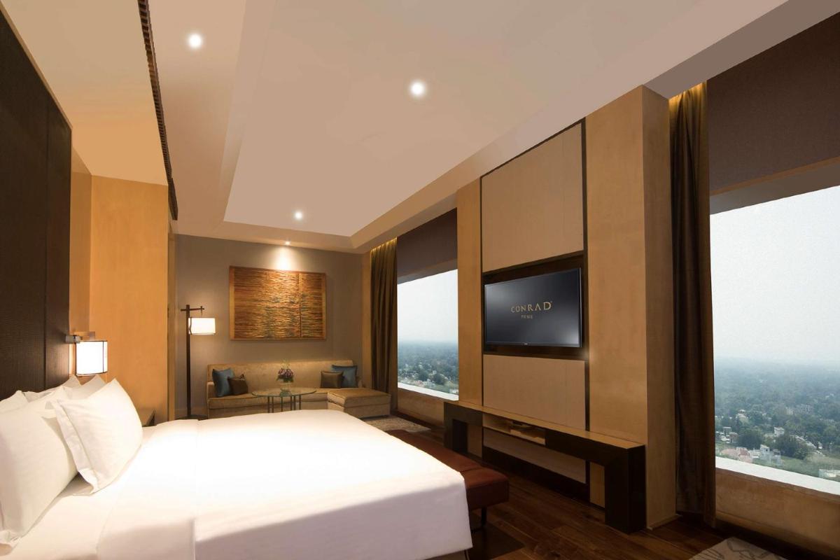 a hotel room with a bed and a flat screen tv at Conrad Pune in Pune