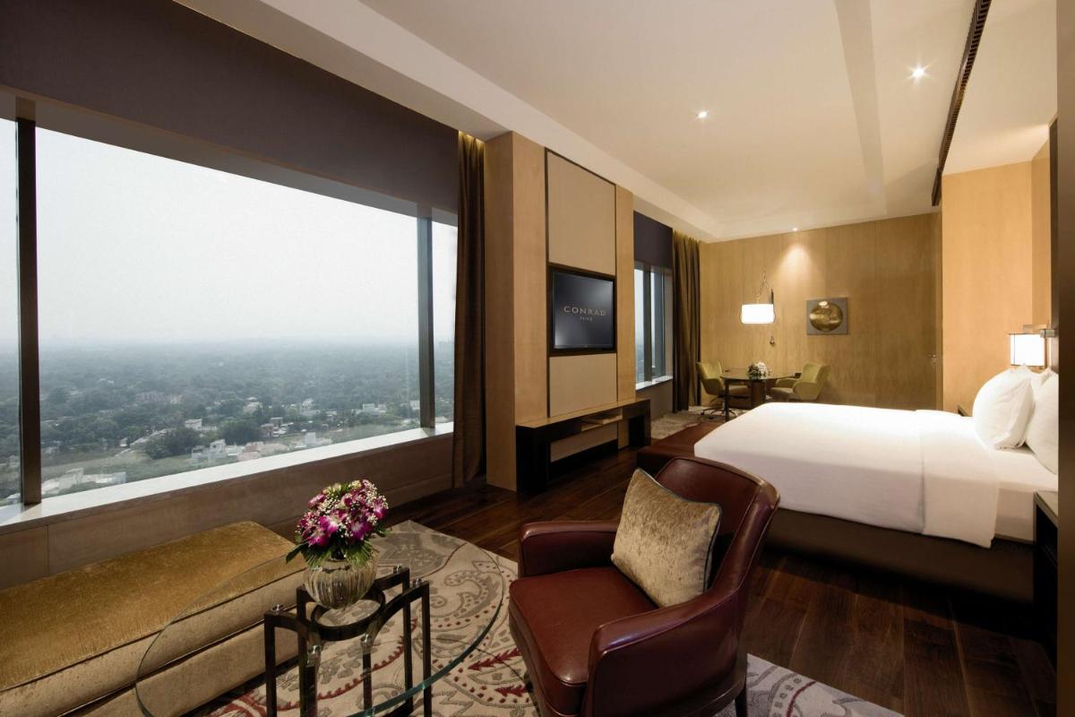a hotel room with a bed and a large window at Conrad Pune in Pune