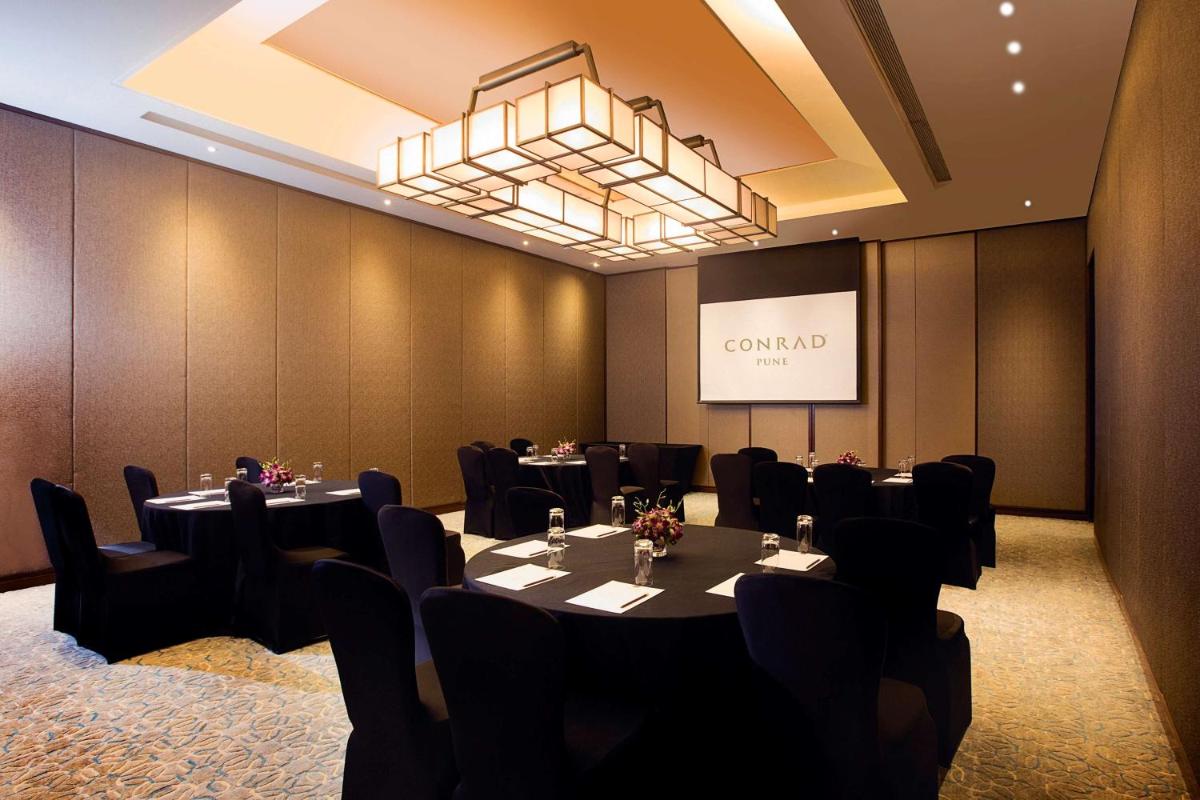 a conference room with tables and chairs and a screen at Conrad Pune in Pune