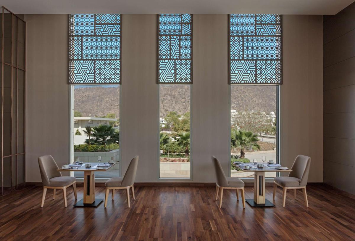a dining room with two tables and chairs and windows at DoubleTree By Hilton Jaipur Amer in Jaipur