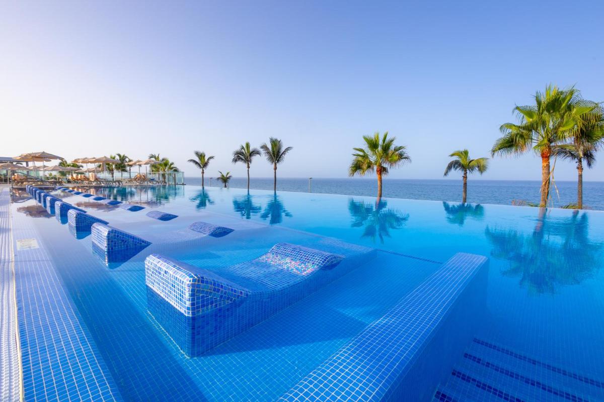 una piscina con palmeras y el océano en Hotel Riu Gran Canaria - All Inclusive, en Maspalomas