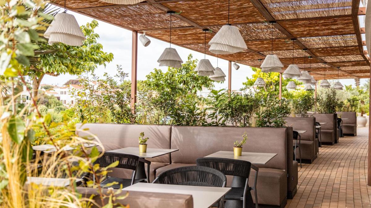Un restaurante con mesas, sillas y plantas. en Seth Port Ciutadella, en Ciutadella