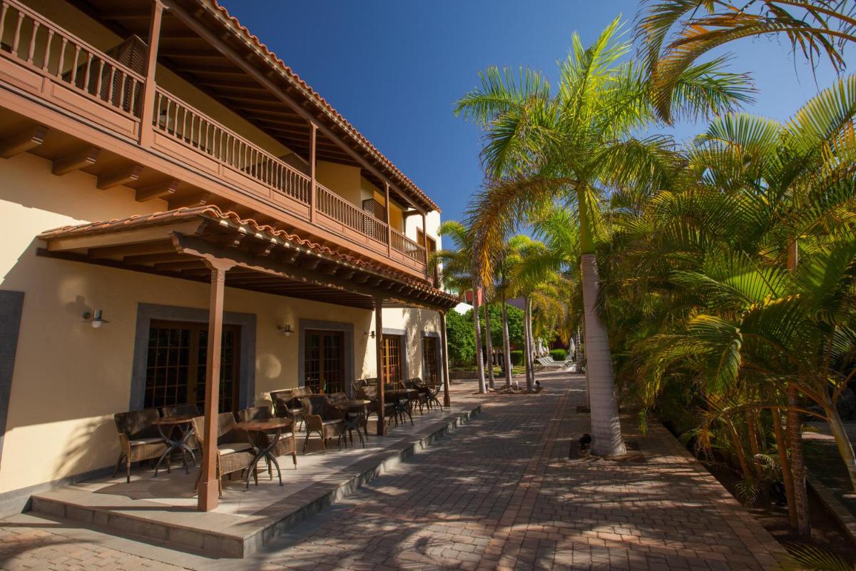 un edificio con mesas, sillas y palmeras en Lopesan Villa del Conde Resort & Thalasso, en Meloneras