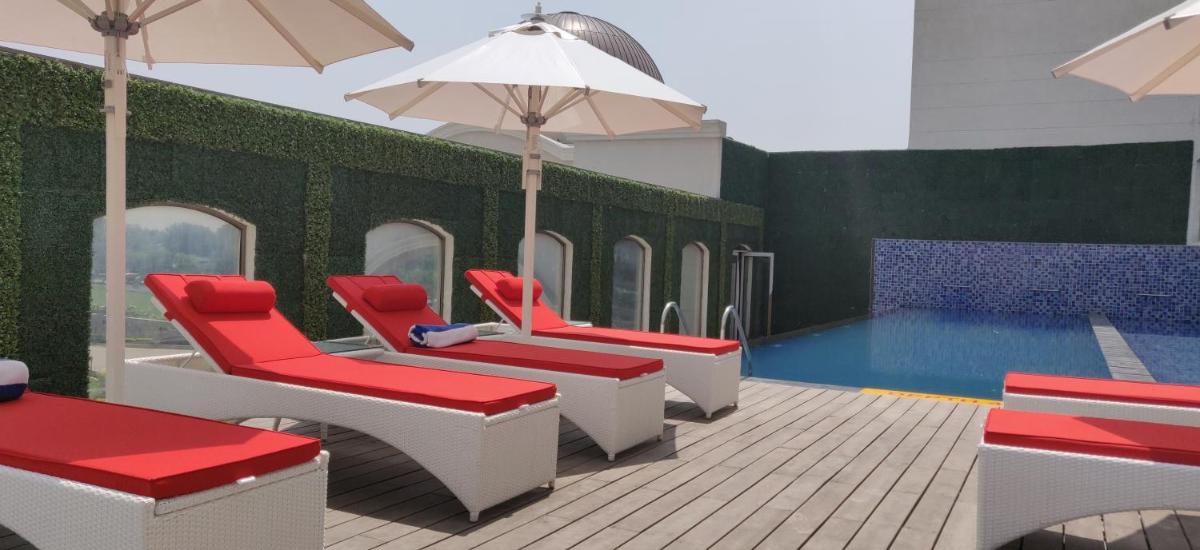 a pool with red and white chairs and an umbrella at Ramada Plaza by Wyndham Lucknow in Lucknow