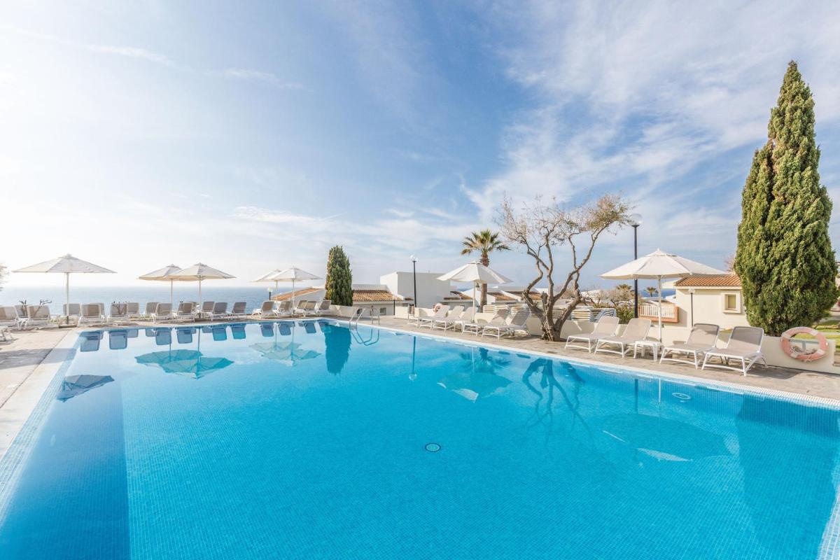 Una gran piscina azul con sillas y sombrillas. en Blau Punta Reina, en Cala Mendia