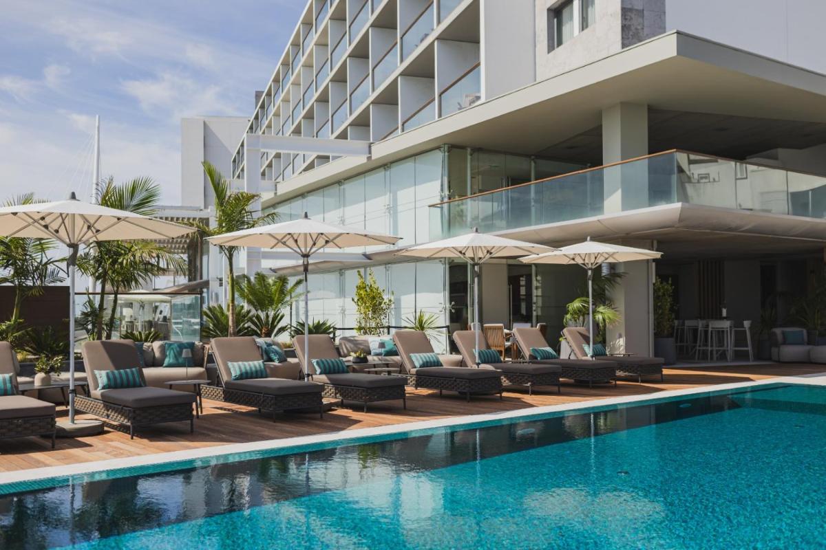 uma piscina com cadeiras e guarda-sóis ao lado de um prédio em Hotel Marina Atlântico em Ponta Delgada