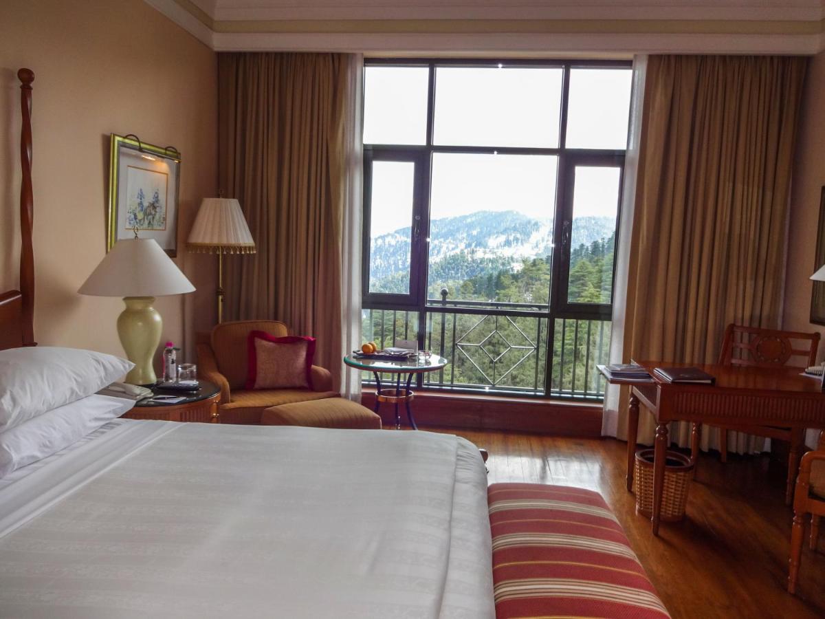 a hotel room with a bed and a large window at Wildflower Hall, An Oberoi Resort, Shimla in Shimla