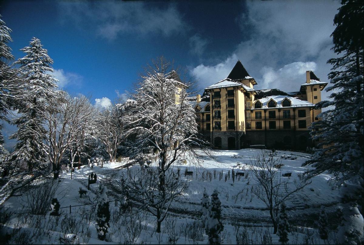 a large building with snow covered trees in front of it at Wildflower Hall, An Oberoi Resort, Shimla in Shimla