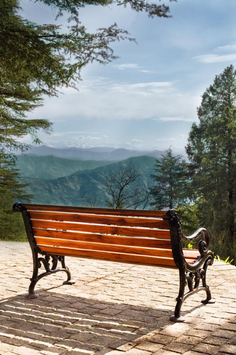 a wooden bench sitting on top of a mountain at Wildflower Hall, An Oberoi Resort, Shimla in Shimla