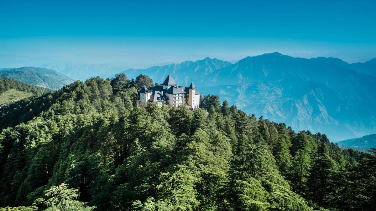 a castle on top of a tree covered mountain at Wildflower Hall, An Oberoi Resort, Shimla in Shimla