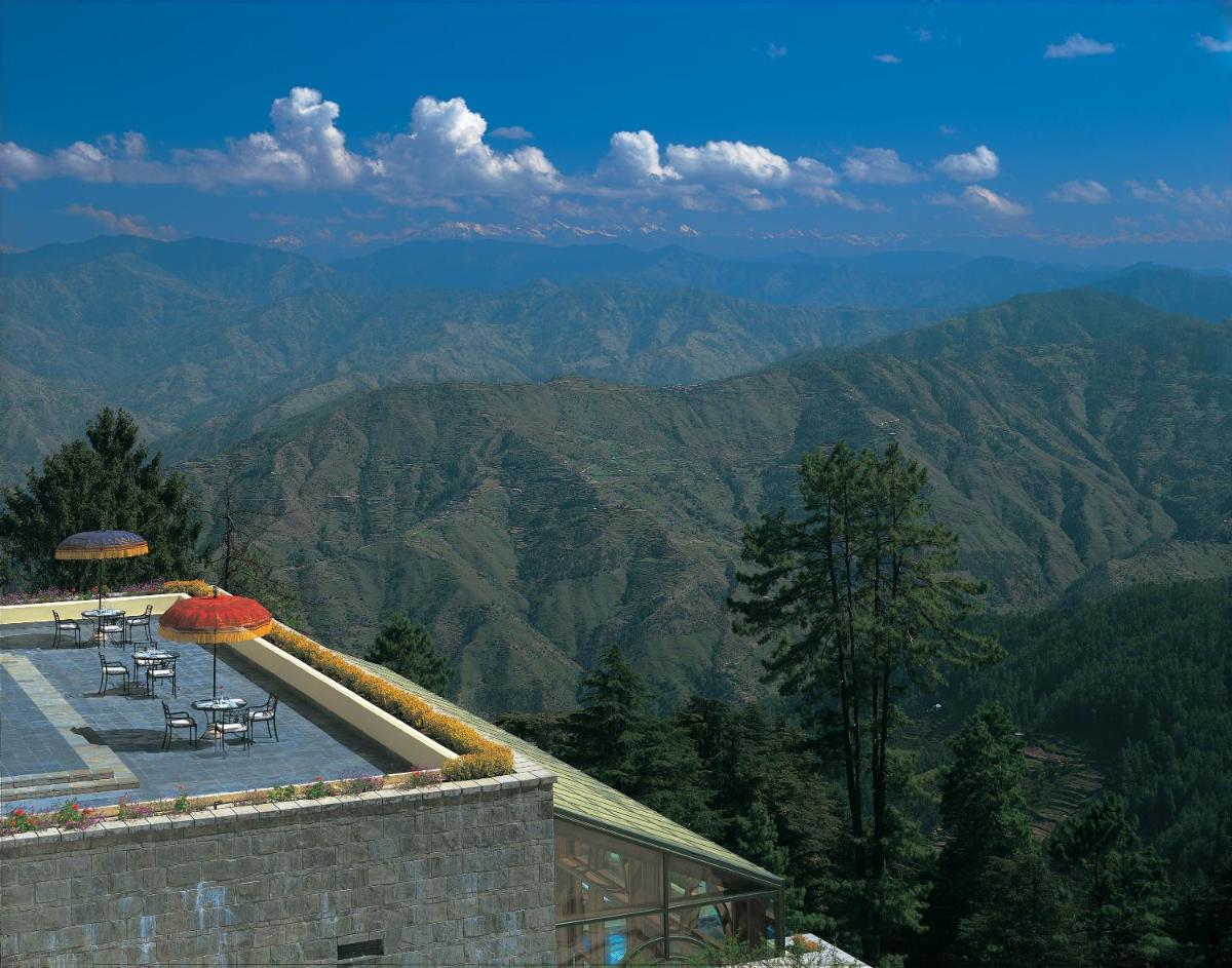 a patio with chairs and an umbrella on top of a mountain at Wildflower Hall, An Oberoi Resort, Shimla in Shimla
