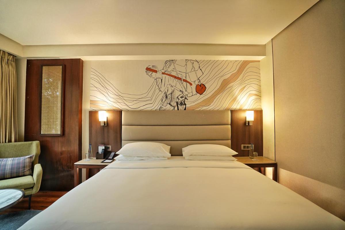 a bedroom with a large white bed and a chair at Hyatt Centric Rajpur Road Dehradun in Dehradun