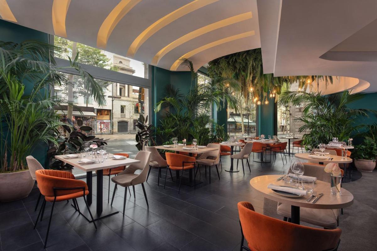 Un restaurante con mesas, sillas y plantas. en Le Meridien Barcelona, en Barcelona