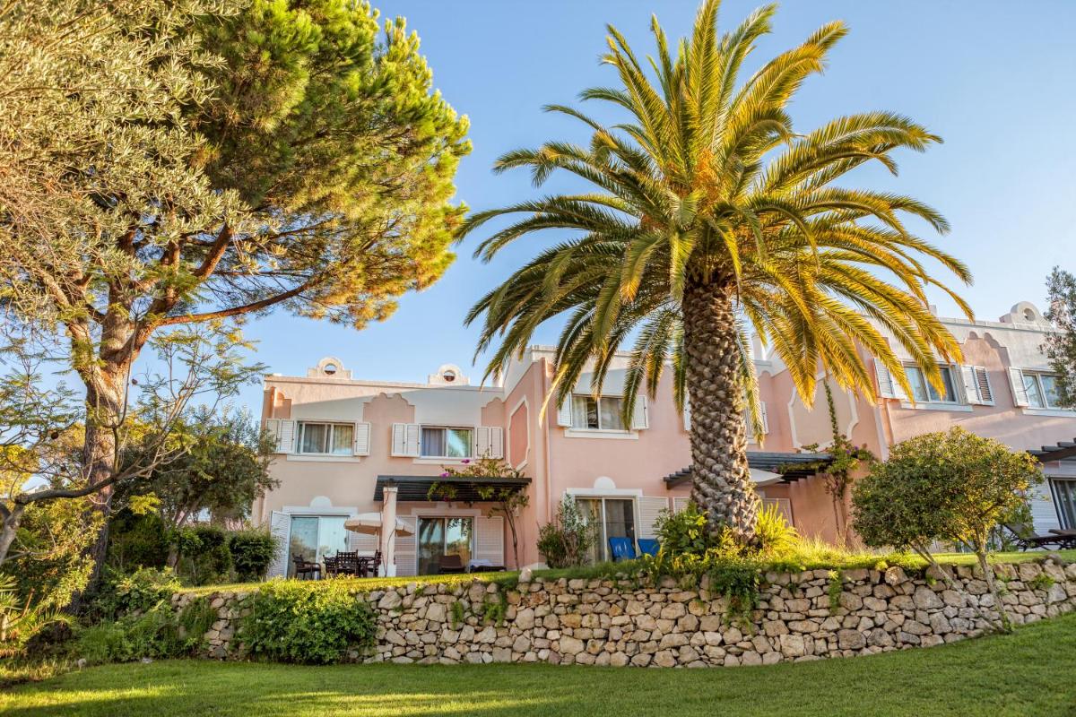 uma casa rosa com palmeiras e uma parede de pedra em Vilar do Golf na Quinta do Lago