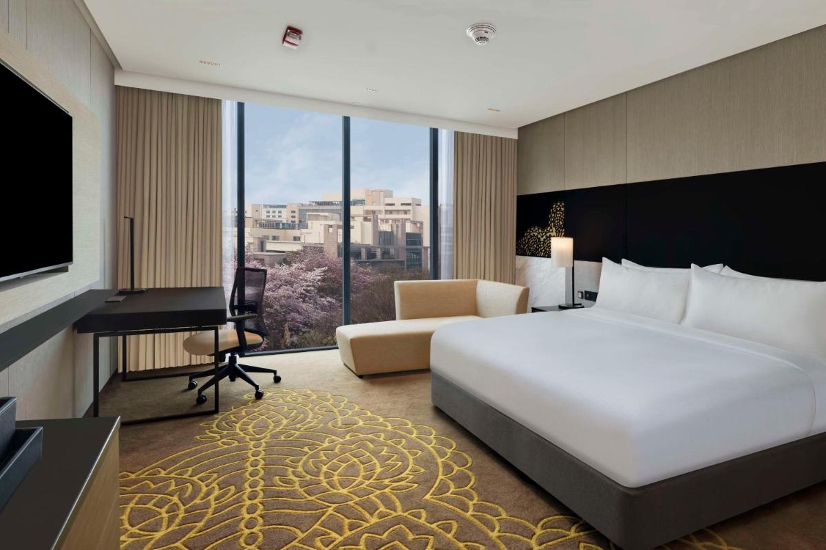 a bedroom with a bed and a desk and a television at Hilton Bengaluru Embassy Manyata Business Park in Bengaluru