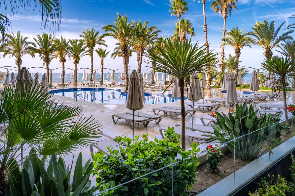 Una vista de una piscina con palmeras y sombrillas. en Caprici Beach Hotel & Spa, en Santa Susanna