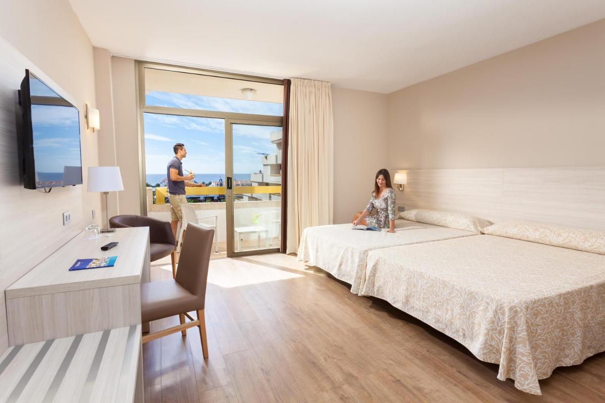 Una mujer sentada en una cama en una habitación de hotel. en Hotel Best Tenerife, en Playa de las Américas