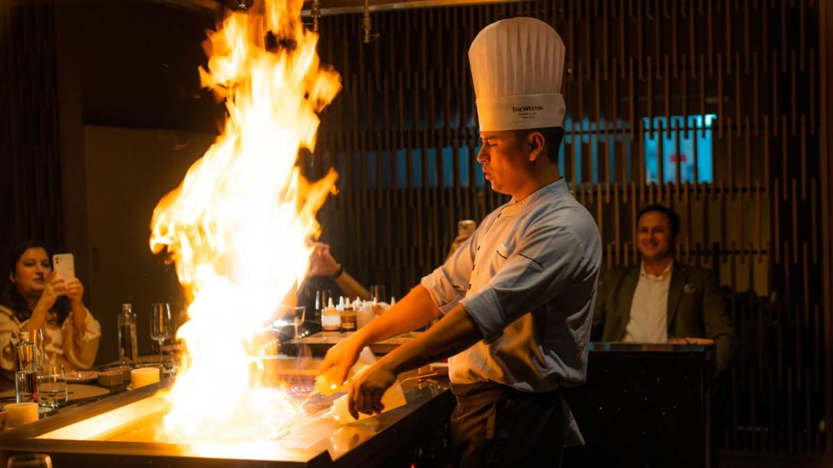 a chef is preparing food in a kitchen with flames at The Westin Resort & Spa Himalayas in Rishīkesh