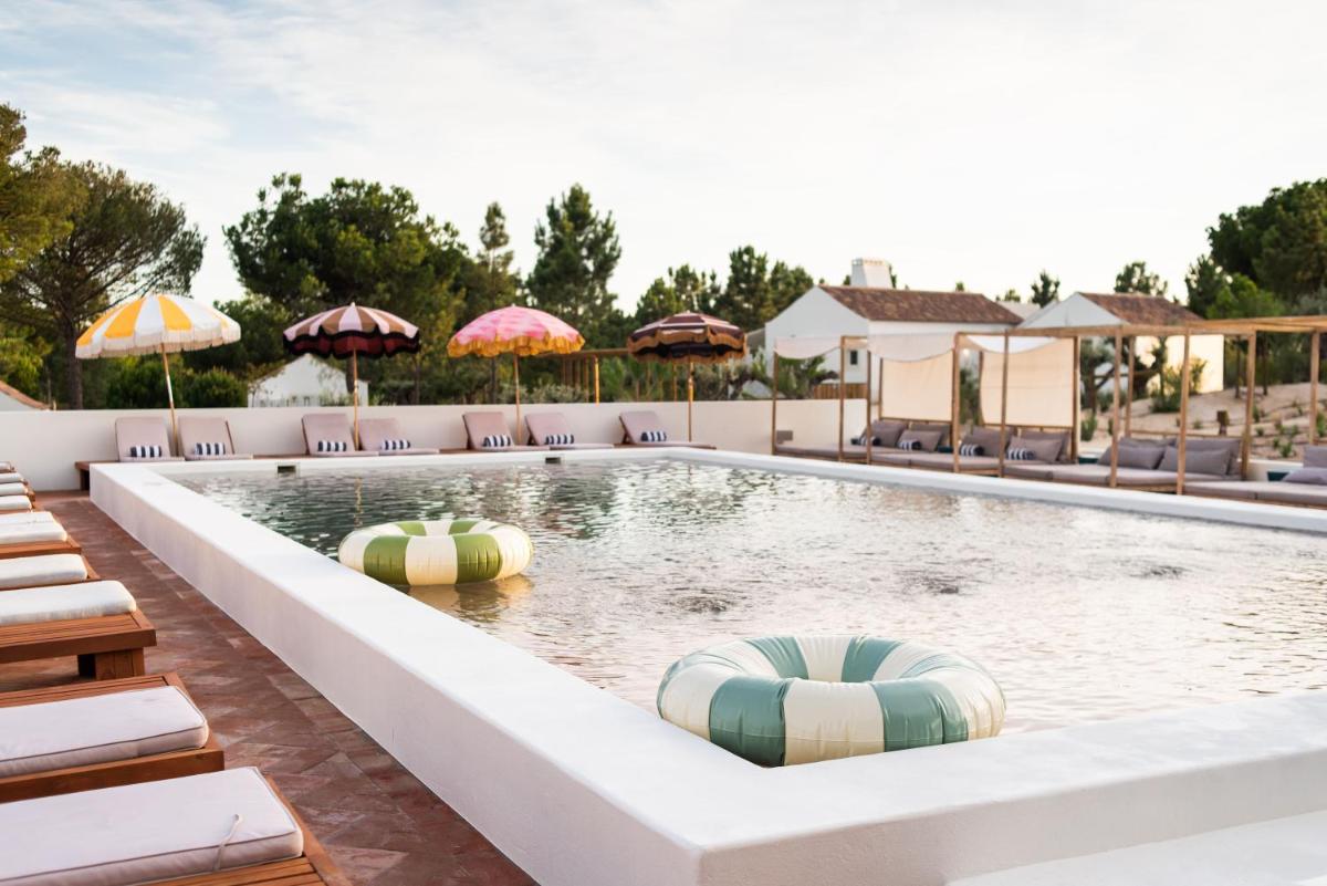 uma piscina com espreguiçadeiras e guarda-sóis em Independente Comporta na Comporta
