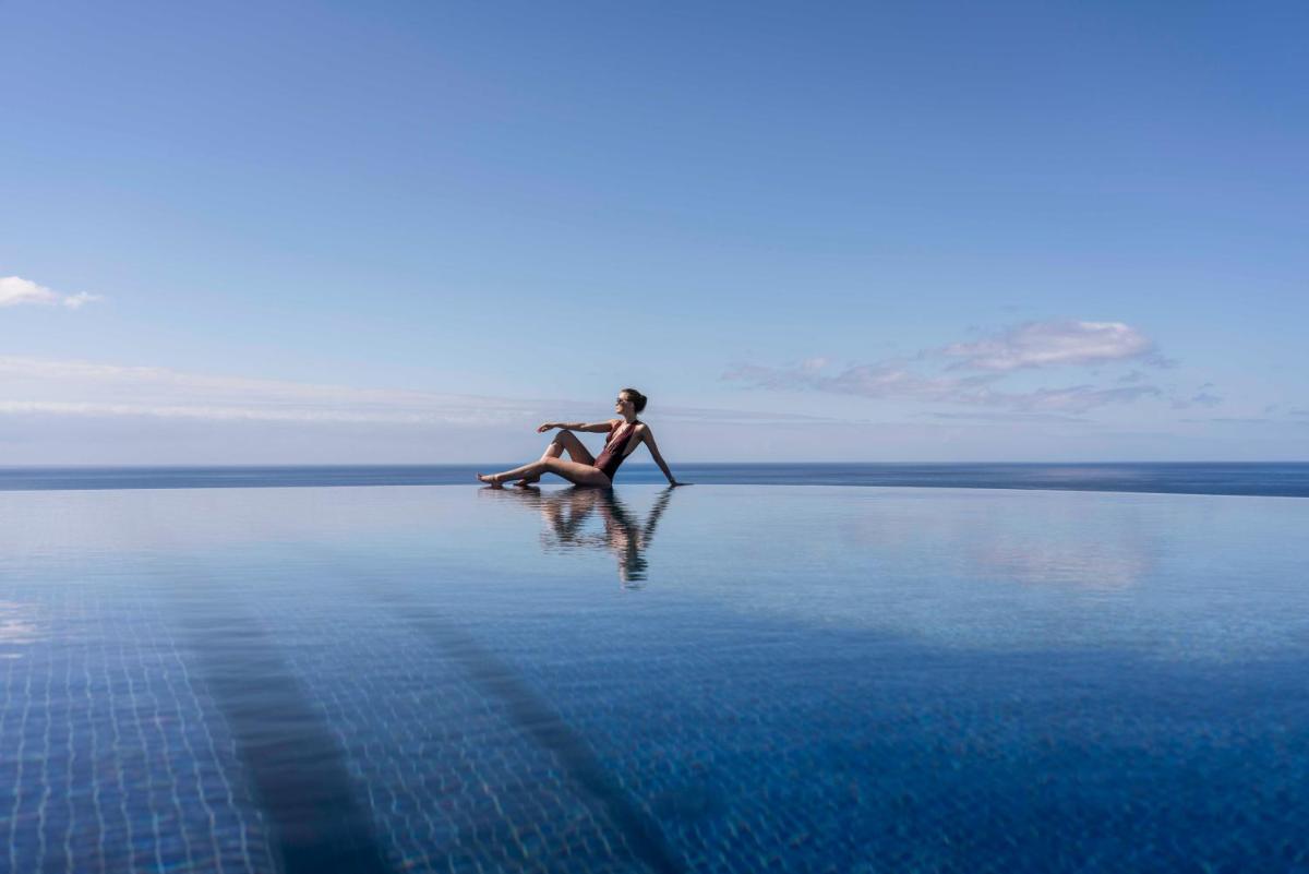 uma mulher sentada numa rocha no meio da água em The Reserve - within Savoy Palace - The Leading Hotels of the World no Funchal