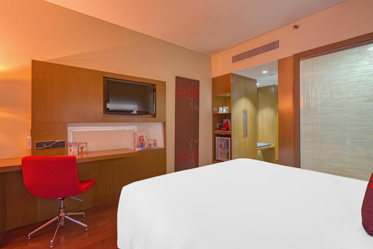 a hotel room with a bed and a red chair at Novotel Bengaluru Outer Ring Road in Bengaluru