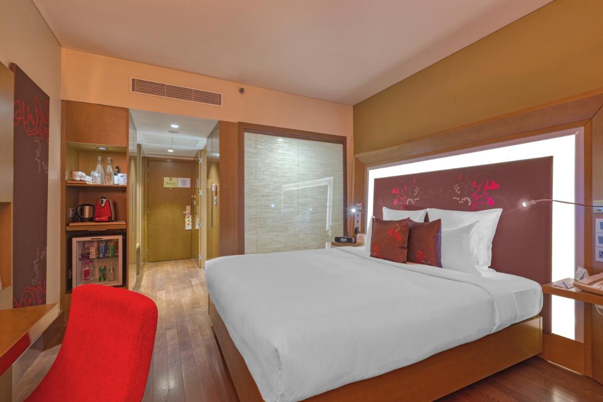 a bedroom with a large bed and a red chair at Novotel Bengaluru Outer Ring Road in Bengaluru