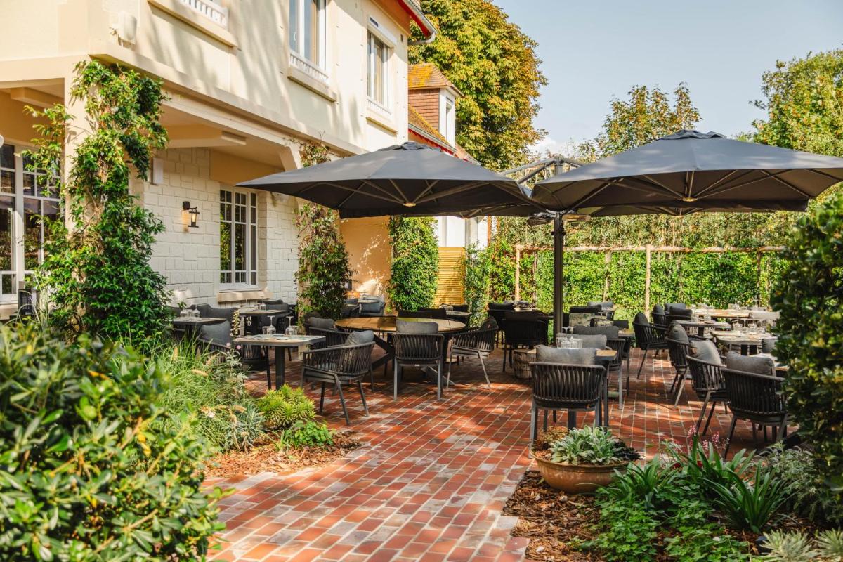 un patio avec tables, chaises et parasols dans l'établissement Le Castel Cabourg hôtel & SPA- Restaurant La Calypso, à Cabourg