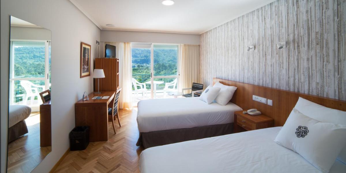 Una habitación de hotel con dos camas y balcón. en ARNOIA CALDARIA HOTEL Y BALNEARIO, en Arnoia