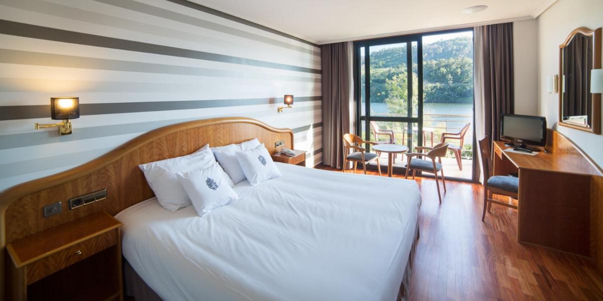 Una habitación de hotel con una cama, un escritorio y un televisor. en Laias Caldaria hotel y Balneario, en Laias