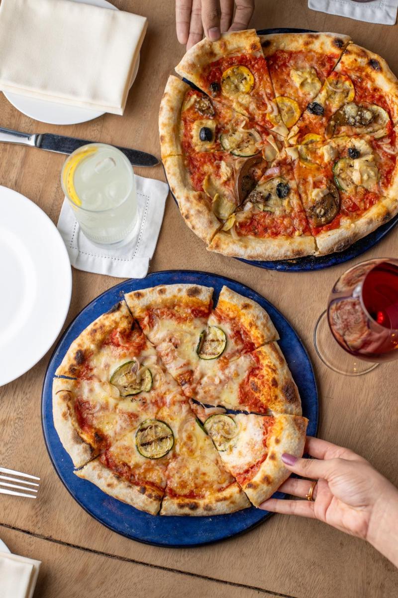 two pizzas on blue plates on a wooden table at Grand Hyatt Gurgaon in Gurgaon