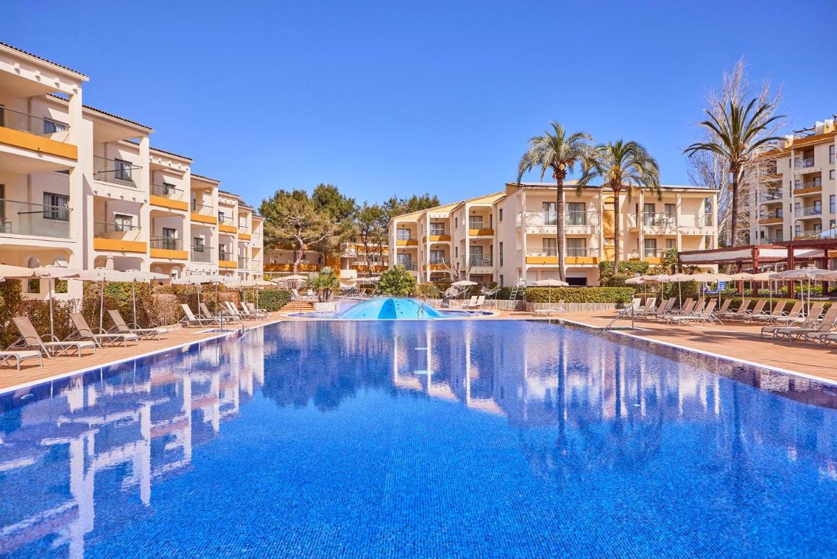 Una piscina en un complejo turístico con palmeras y edificios. en Zafiro Tropic, en Puerto de Alcudia