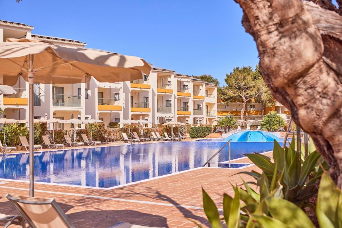 Una piscina en un hotel con sillas y sombrilla. en Zafiro Tropic, en Puerto de Alcudia