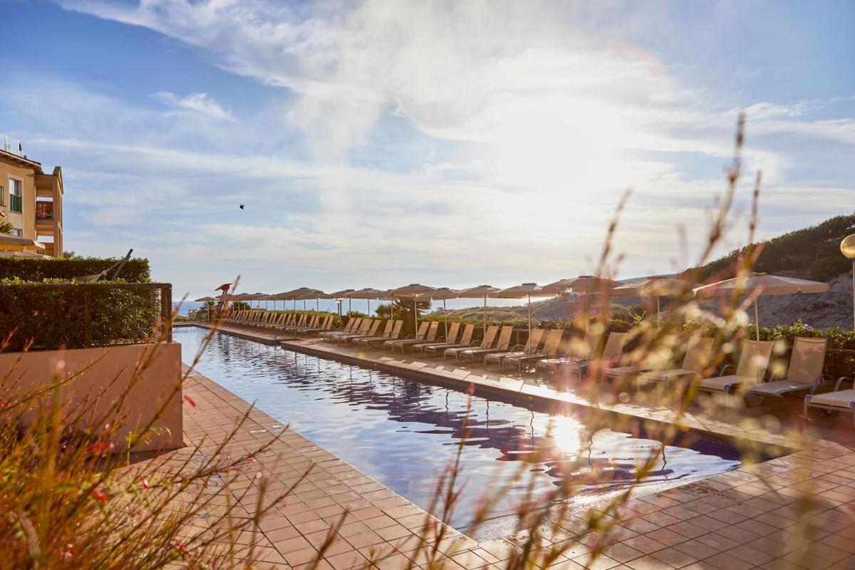 un cuerpo de agua con edificios y el sol en el cielo en Zafiro Cala Mesquida, en Cala Mesquida
