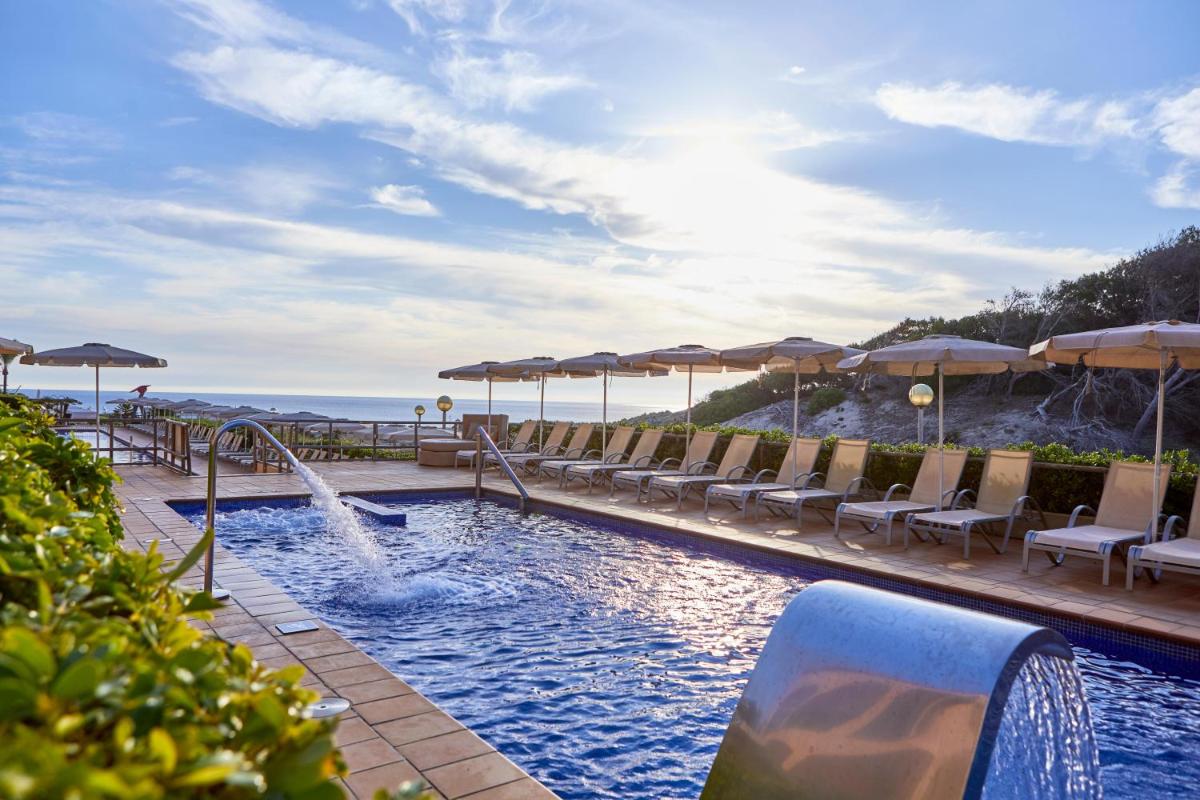 una piscina con sillas y sombrillas en una playa en Zafiro Cala Mesquida, en Cala Mesquida