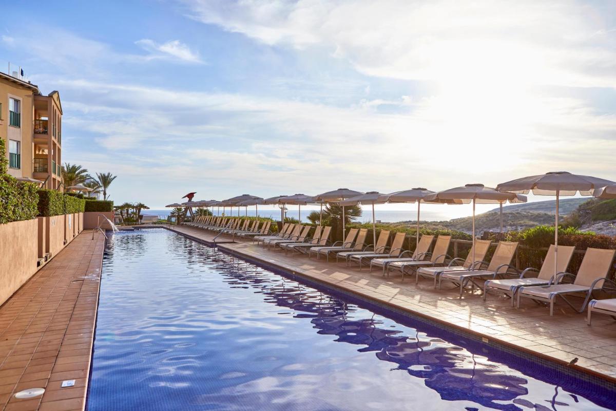 Una piscina con sillas y sombrillas junto al mar. en Zafiro Cala Mesquida, en Cala Mesquida 68 fotos más