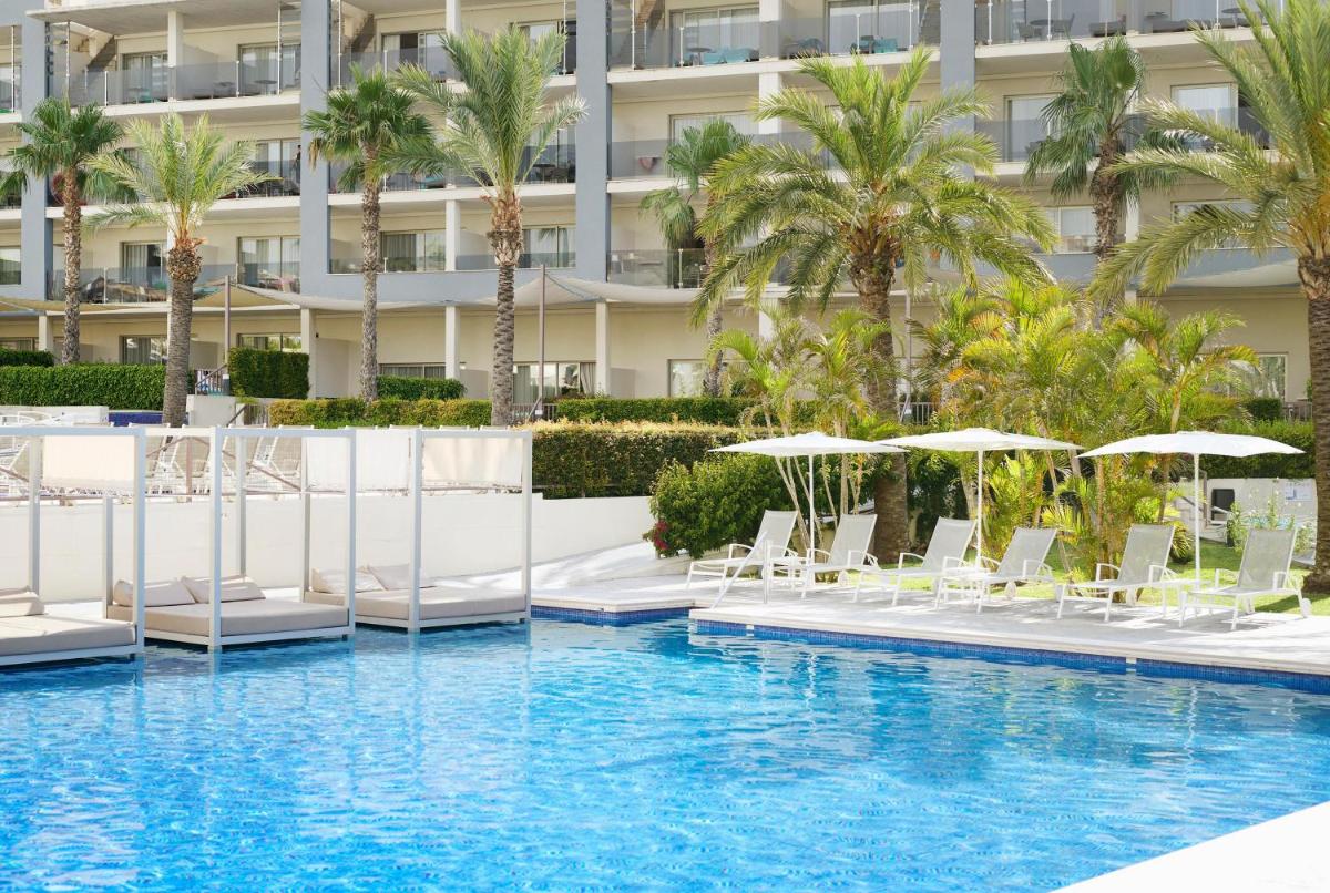 Una piscina con sillas y sombrillas frente a un edificio. en Zafiro Palace Alcudia, en Puerto de Alcudia
