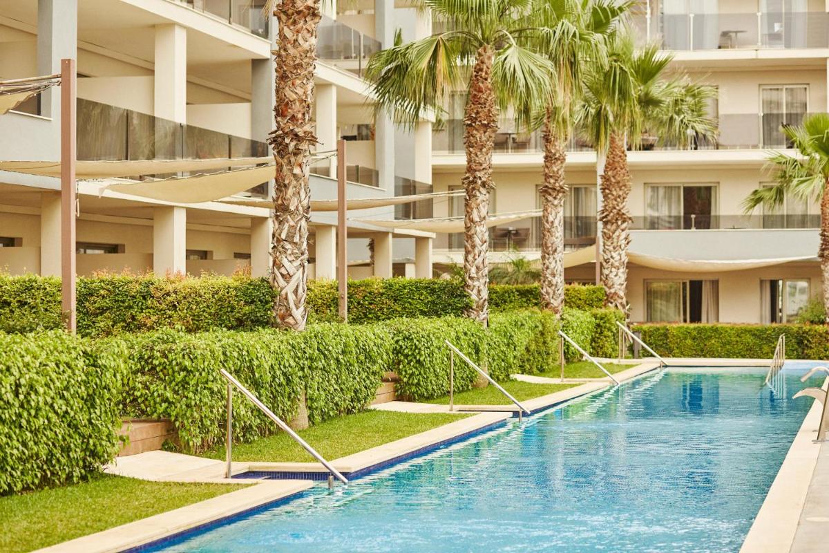 una piscina frente a un edificio con palmeras en Zafiro Palace Alcudia, en Puerto de Alcudia
