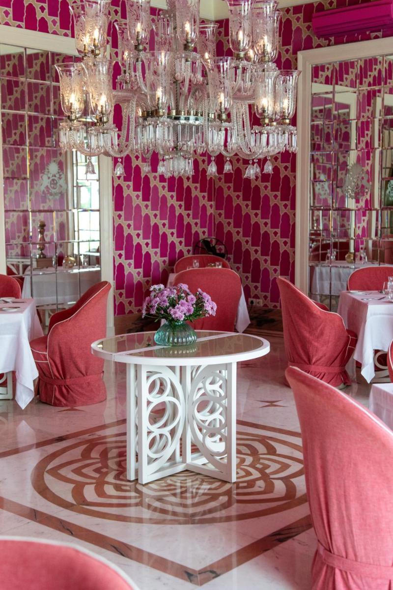 a pink room with a table and chairs and chandeliers at Rajmahal Palace RAAS in Jaipur