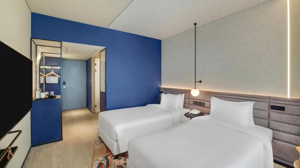 a hotel room with two beds and a blue wall at Novotel Pune Viman Nagar Road in Pune