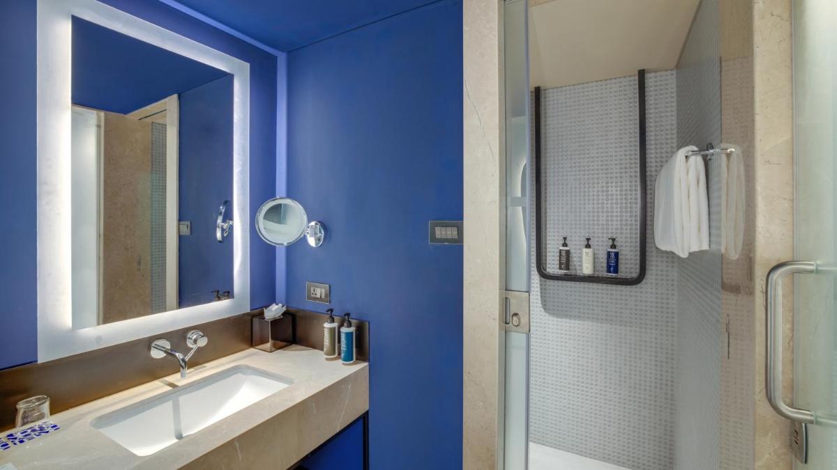 a blue bathroom with a sink and a shower at Novotel Pune Viman Nagar Road in Pune