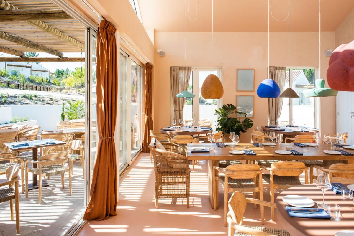 uma sala de jantar com mesas, cadeiras e janelas em Independente Comporta na Comporta