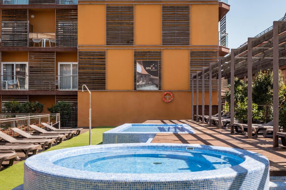 Una piscina al aire libre con sillas y un edificio. en ALEGRIA Plaza Paris 4*Sup, en Lloret de Mar